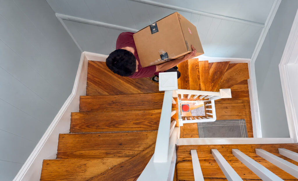 Mover carrying a moving box down a clear staircase on moving day