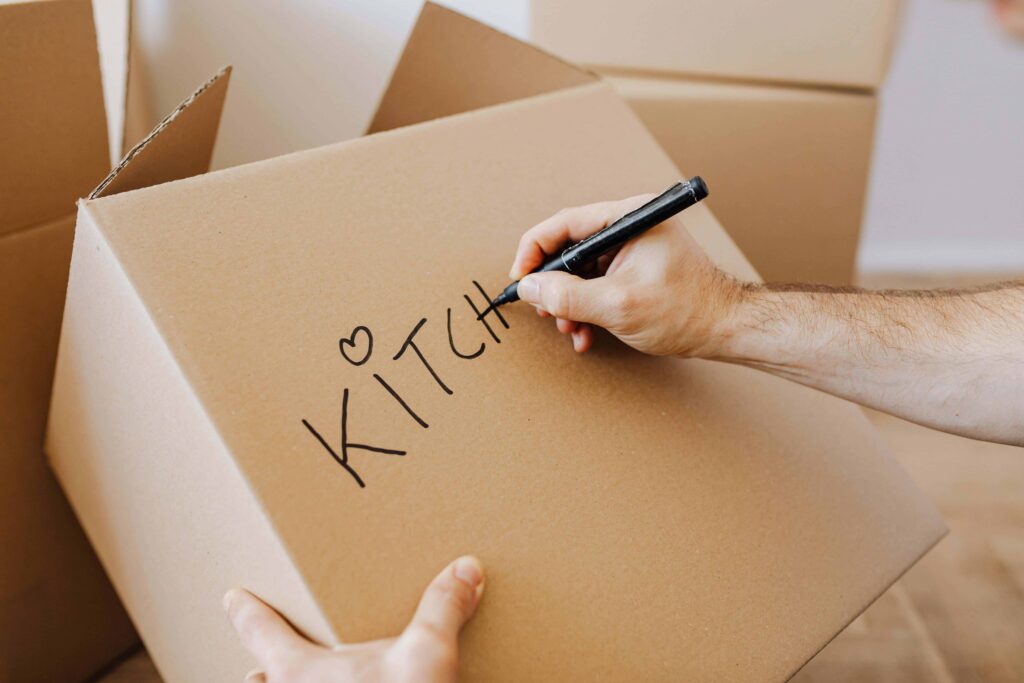 Labeling a moving box by room with a marker before movers arrive