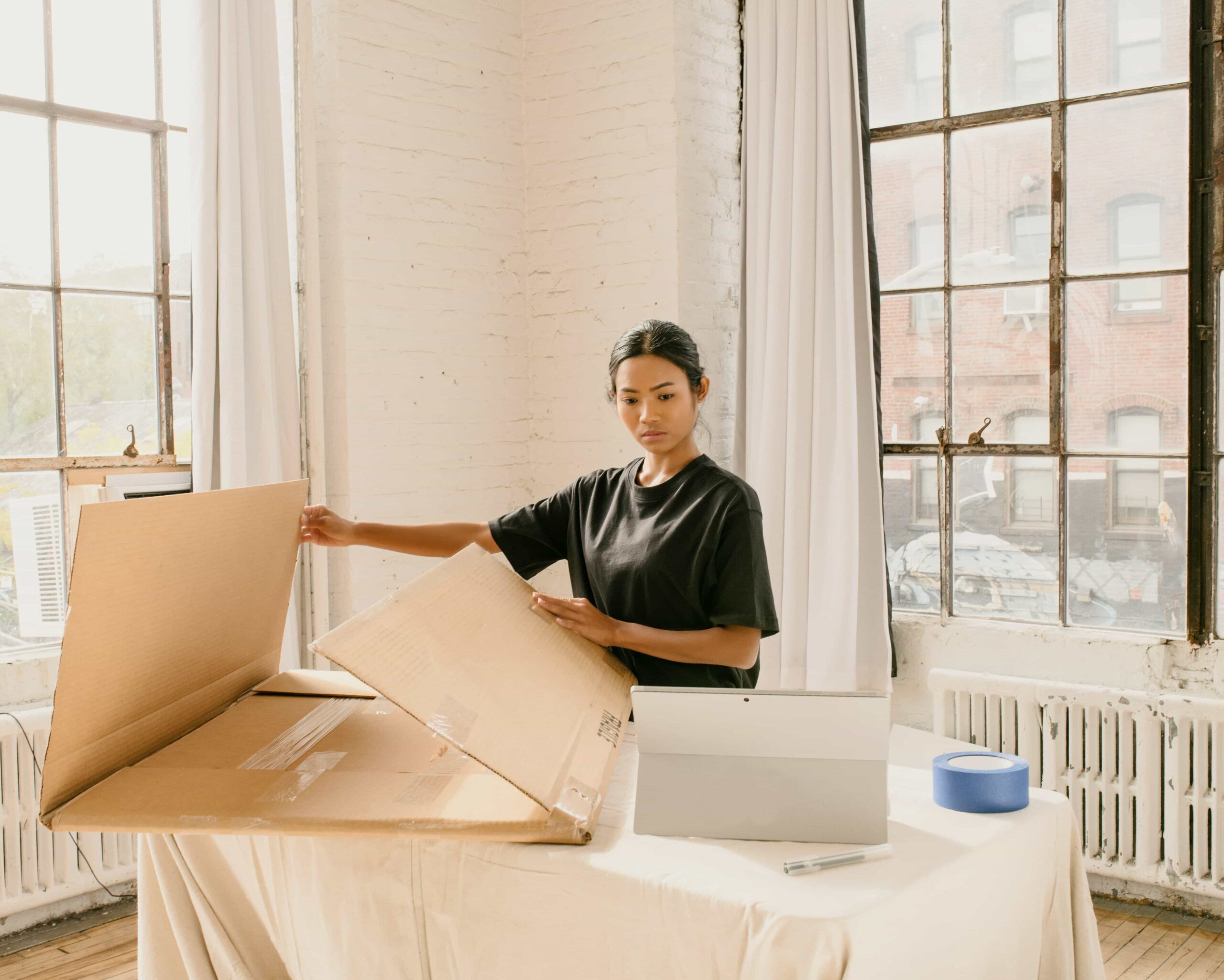 Woman assembling a moving box next to her laptop while updating her address before a move
