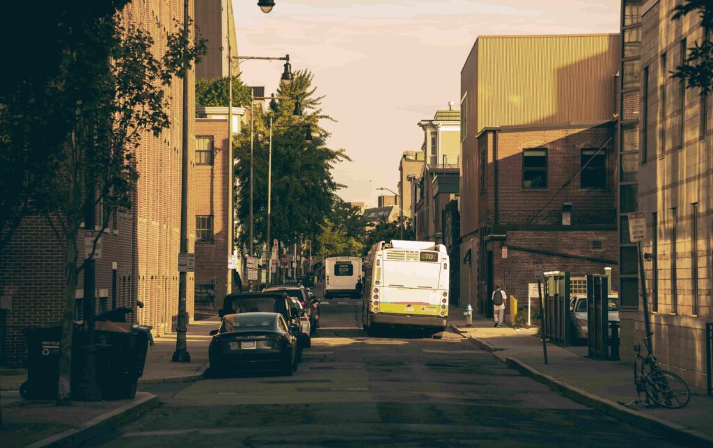Narrow Cambridge street near Central Square with parked cars and a city bus, where truck routing takes experience