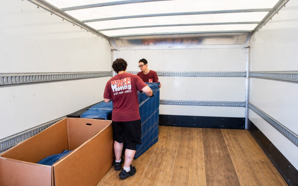 Better Call Moving crew securing blanket-wrapped furniture against the wall rails of a clean truck