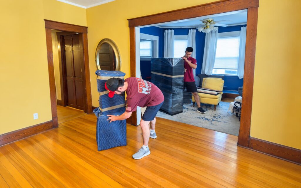 Better Call Moving crew protecting tall furniture with stretch wrap and moving blankets in a client’s home