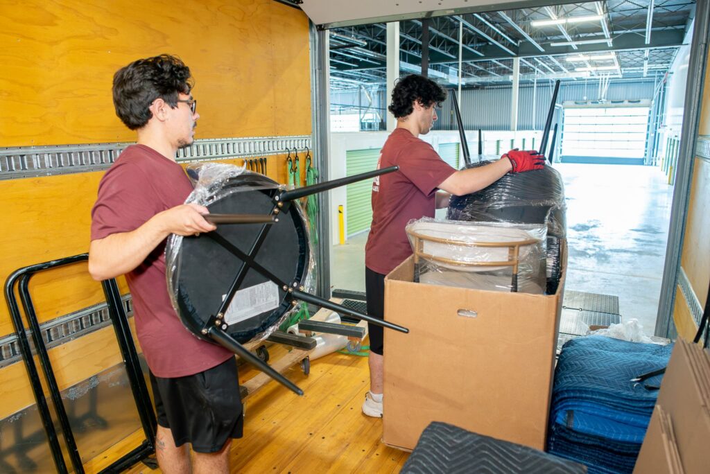 Two-person moving crew loading wrapped furniture into the truck with dollies and blankets